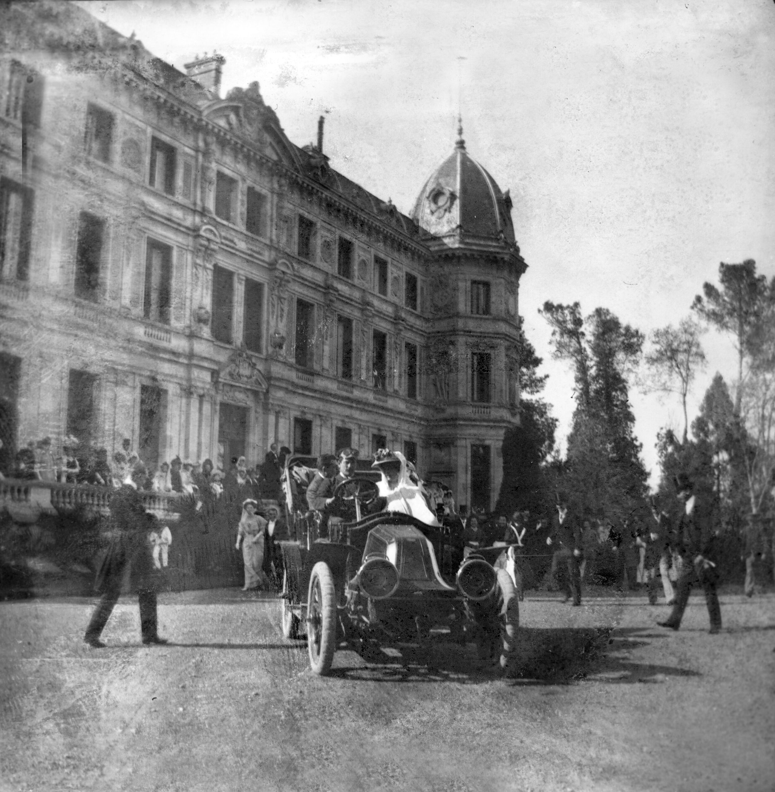 Grupo de invitados frente al Recreo de las Cadenas durante una boda en 1907, con un automóvil antiguo en primer plano.
